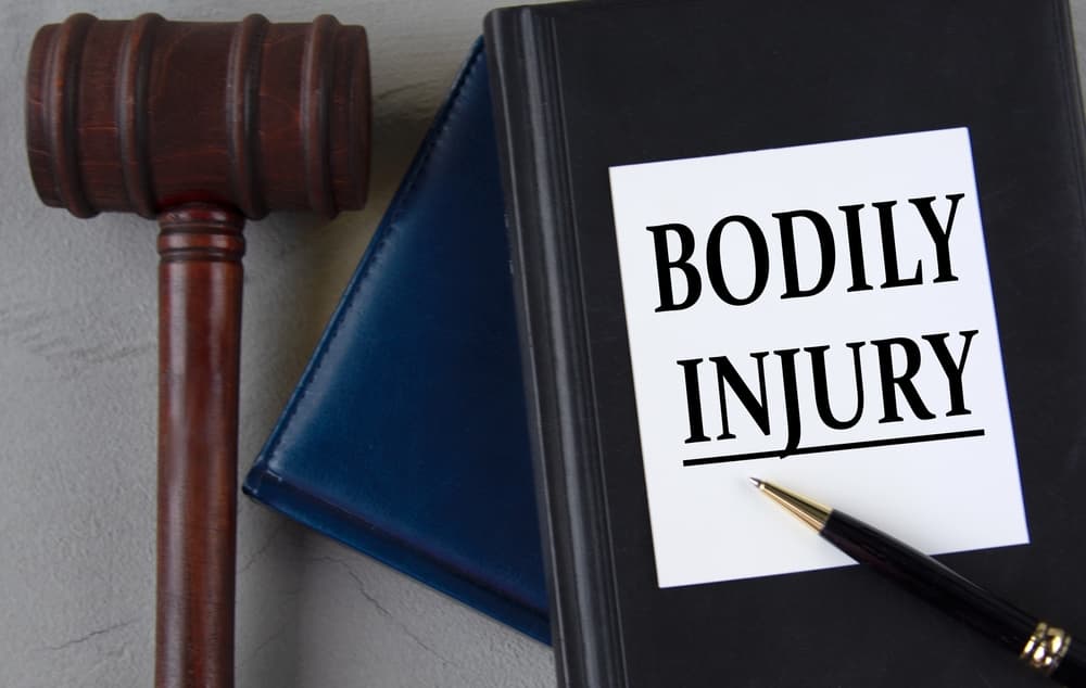 BODILY INJURY - words on a white sheet with leather notebooks, a judge's hammer and a pen