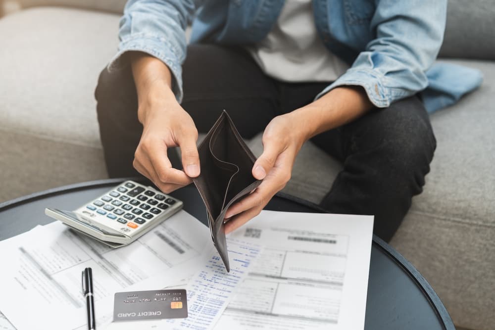 A financial hardship concept featuring a stressed Asian man holding an open, empty wallet, showing a lack of money and credit cards, symbolizing struggles with debt and inability to make payments.